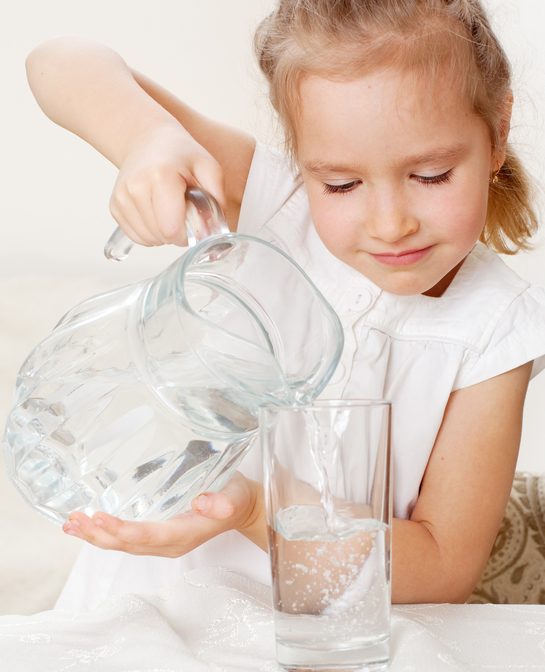 Child with glass pitcher water. Little girl drinking water at home