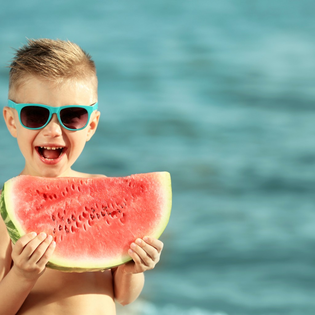 Cute boy eating watermelon on beach